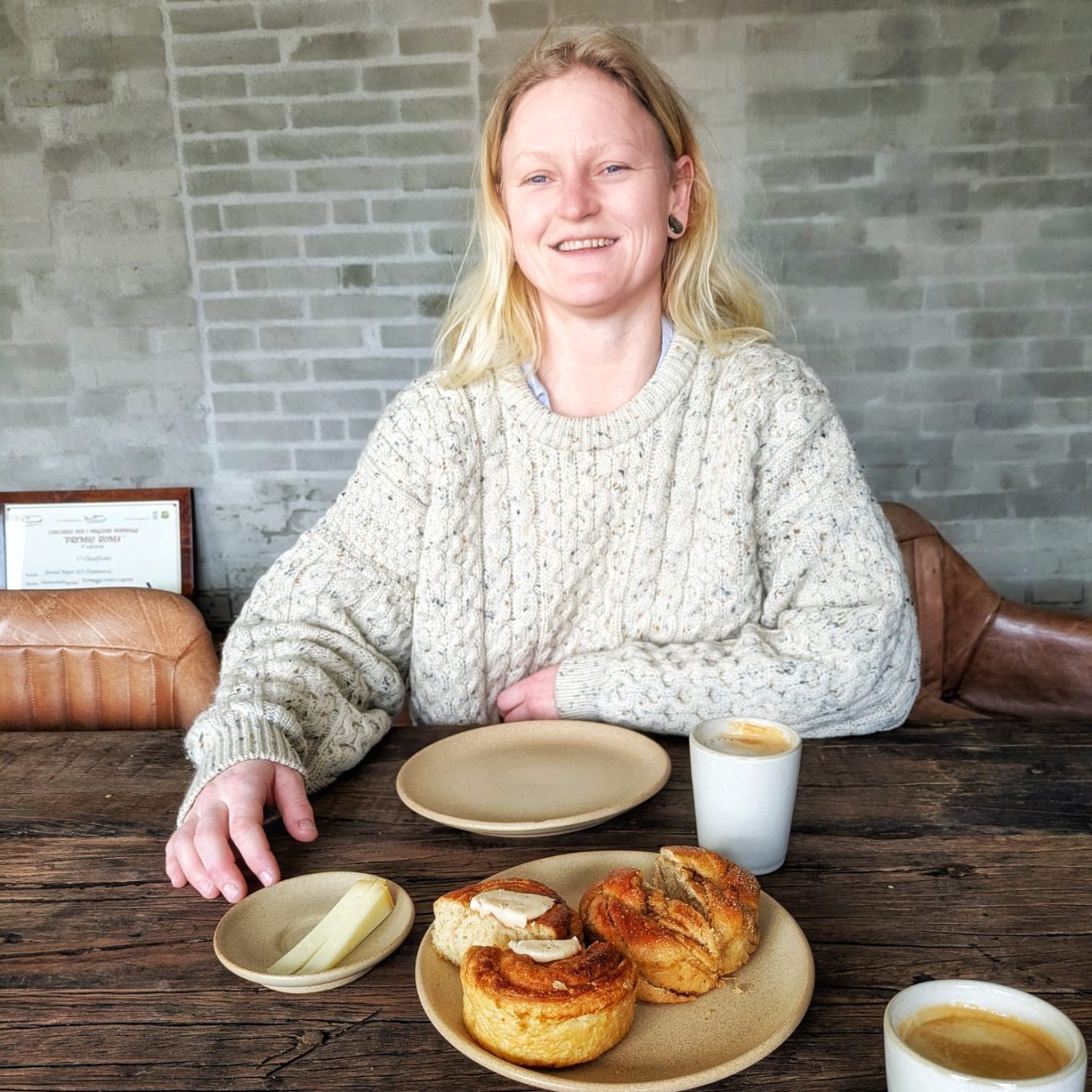 Siri Vilmann sitzt an einem gedeckten Tisch mit einer Tasse Kaffee und Kardamomsnegle und blickt entspannt in die Szene