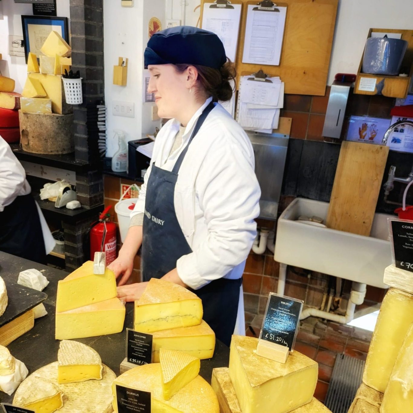 Käsehändlerin Abbey schmunzelt hinter der Theke bei Neal’s Yard Dairy.