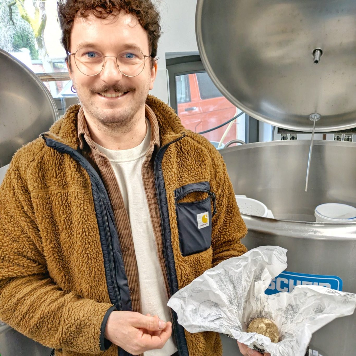 Markus  zeigt seine Interpretation der Belper Knolle in Käserei in der Hand und lacht in die Kamera