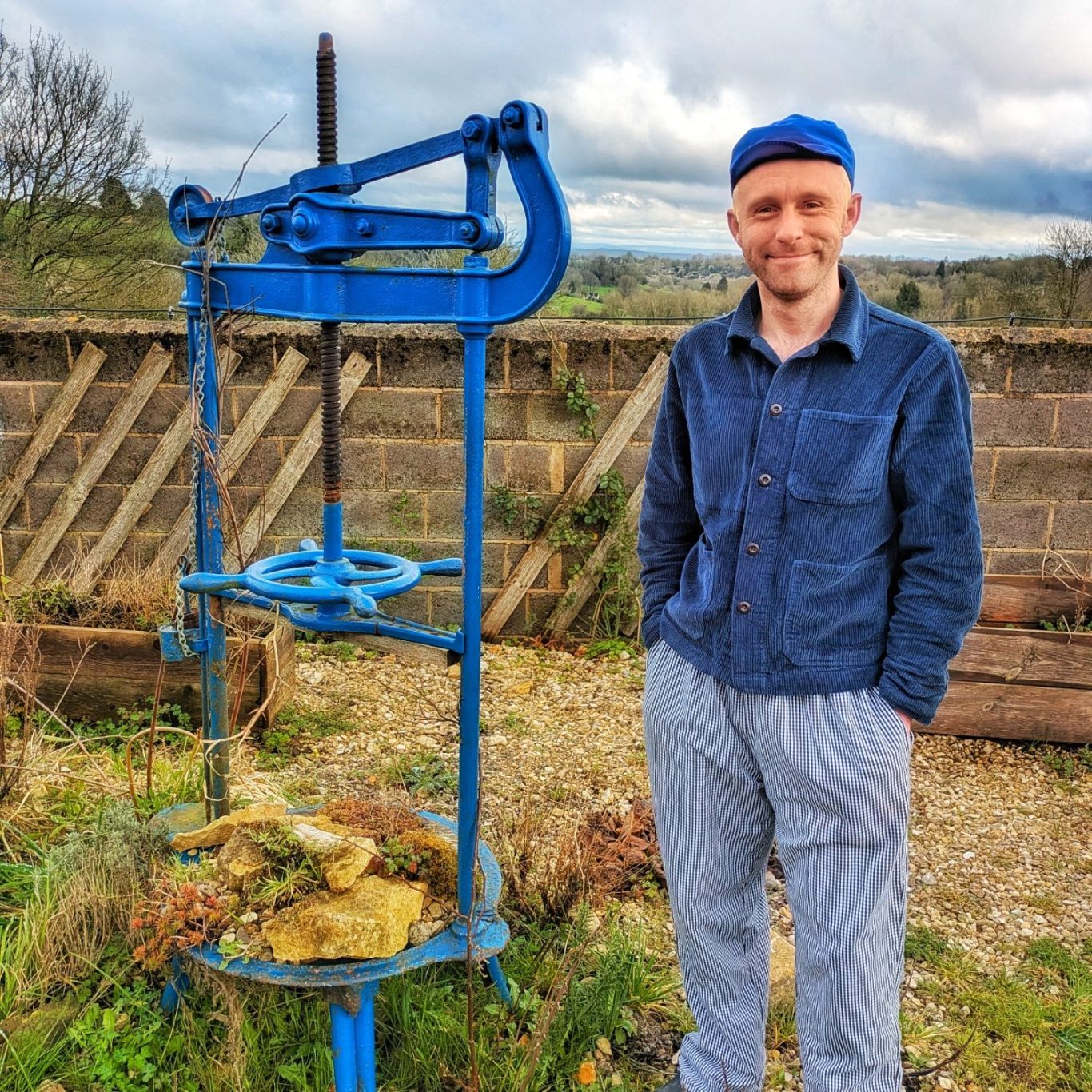 David Jowett steht neben einer alten Käsepresse, im Hintergrund die Hügellandschaft der Cotswolds.