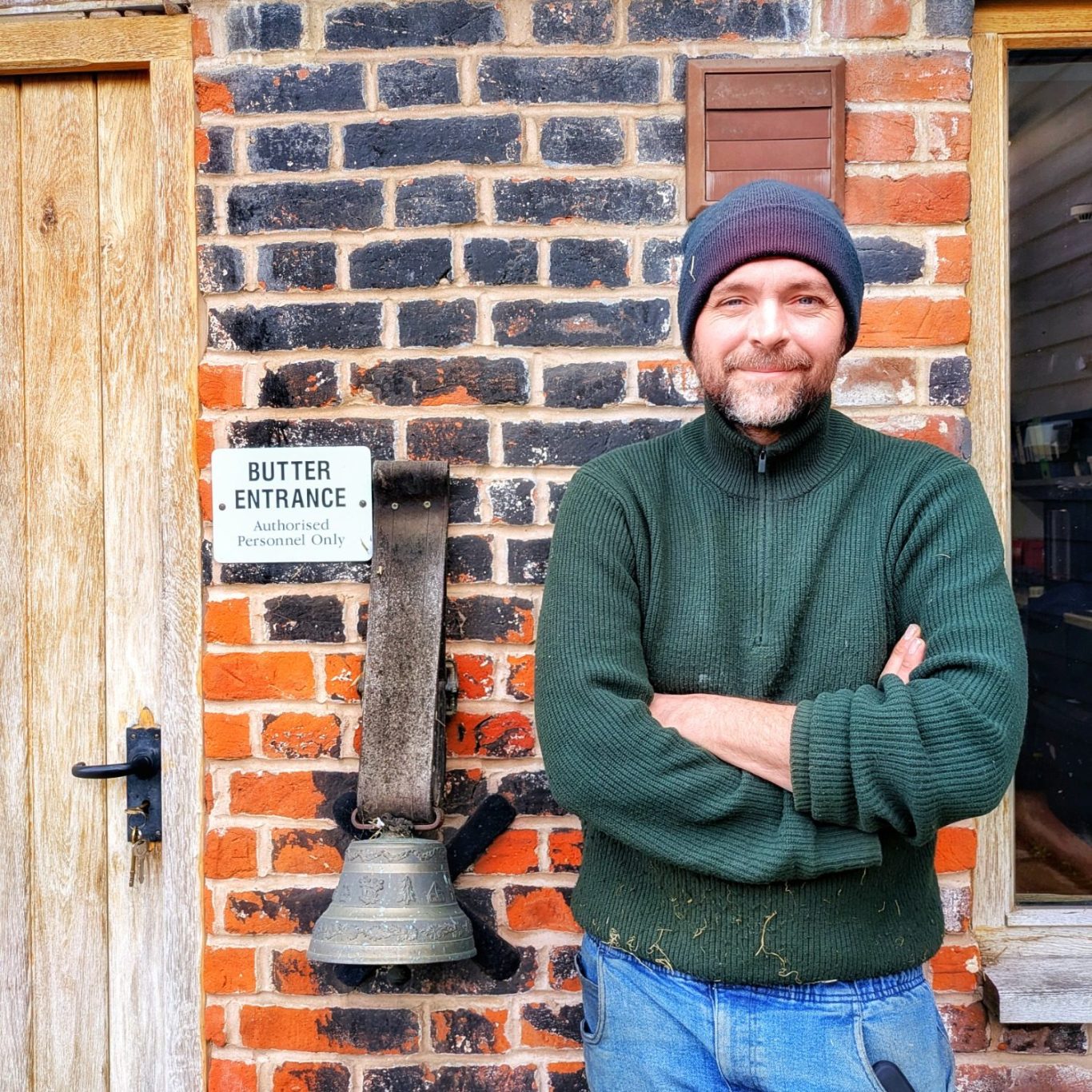 Porträt von Jonny Crickmore im Freien, stehend vor einer Außenwand der Fen Farm Dairy in Suffolk, England.