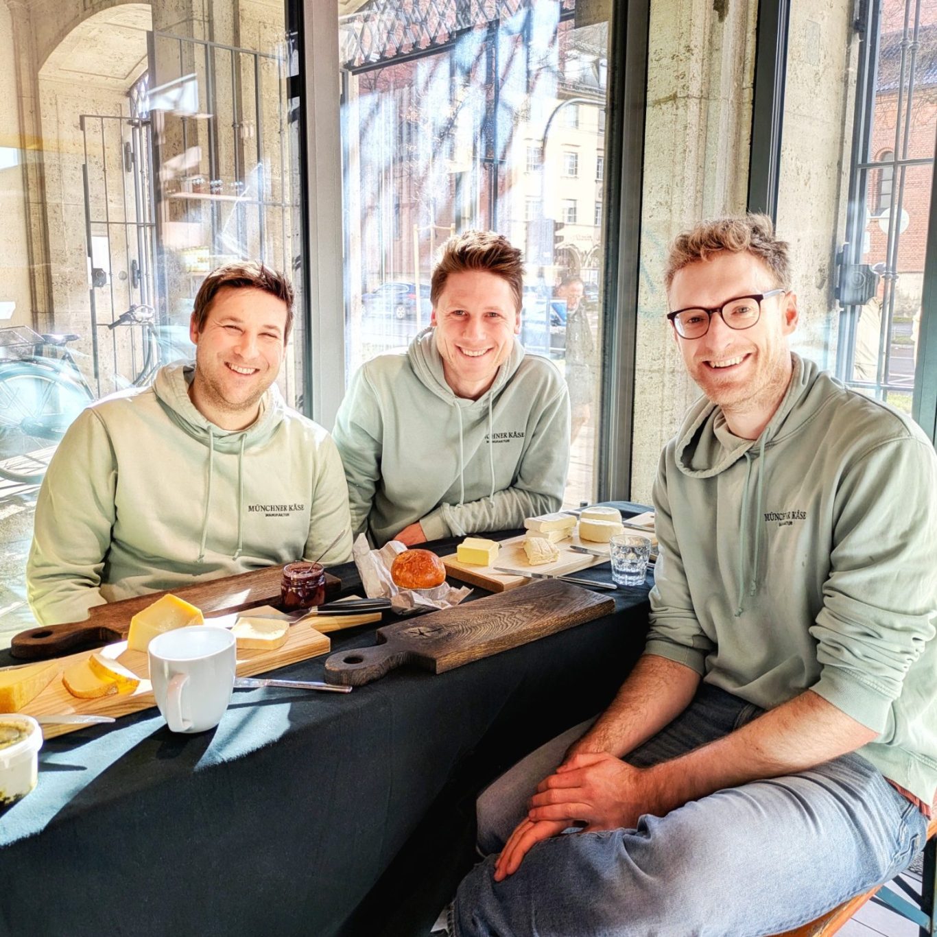 Franz Stuffer, Sebastian Kreuels und Johannes Klappacher sitzen im Verkaufsraum der Münchener Käsemanufaktur