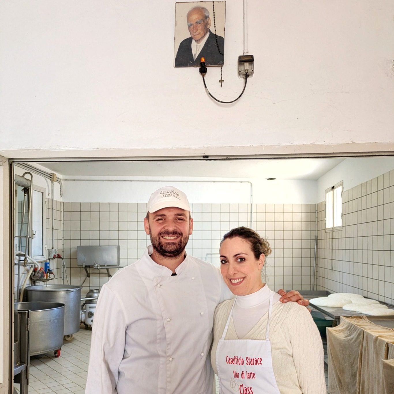 Angela und Antonio Starace stehen in ihrer Käserei; über dem Eingang hängt das Porträt von Giovannis Vater