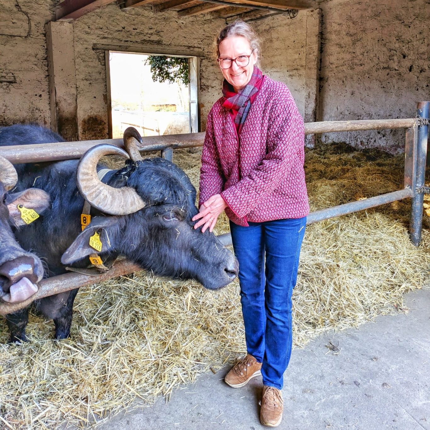 Elke Henrion lacht neben einem Wasserbüffel vor dem Stall auf dem Büffelhof Bobalis in Jüterbog.