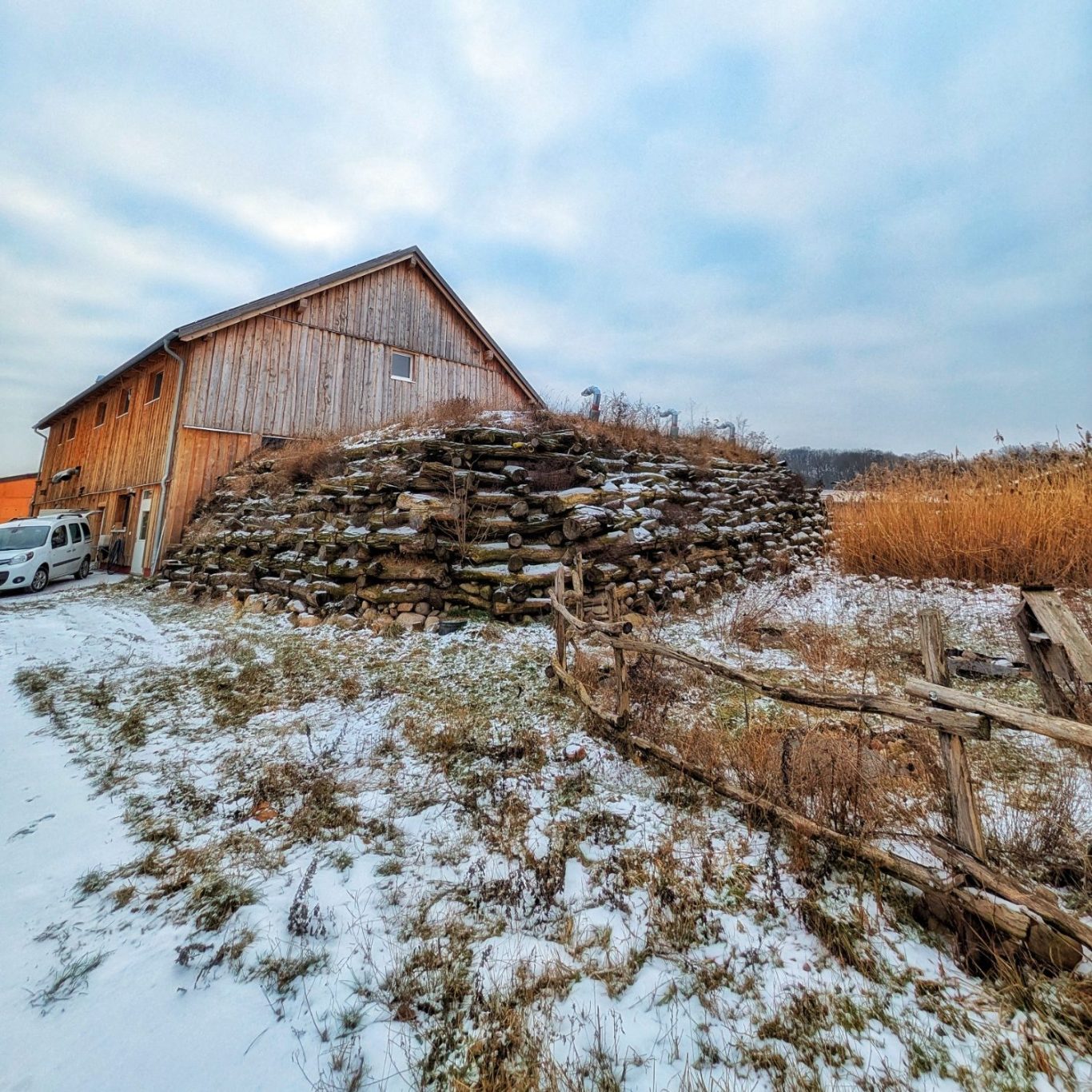 Die Fassade der neuen Käserei auf Gut Ogrosen. Vor dem Gebäude steht eine Krainerwand aus gestapelten Holzstämmen.