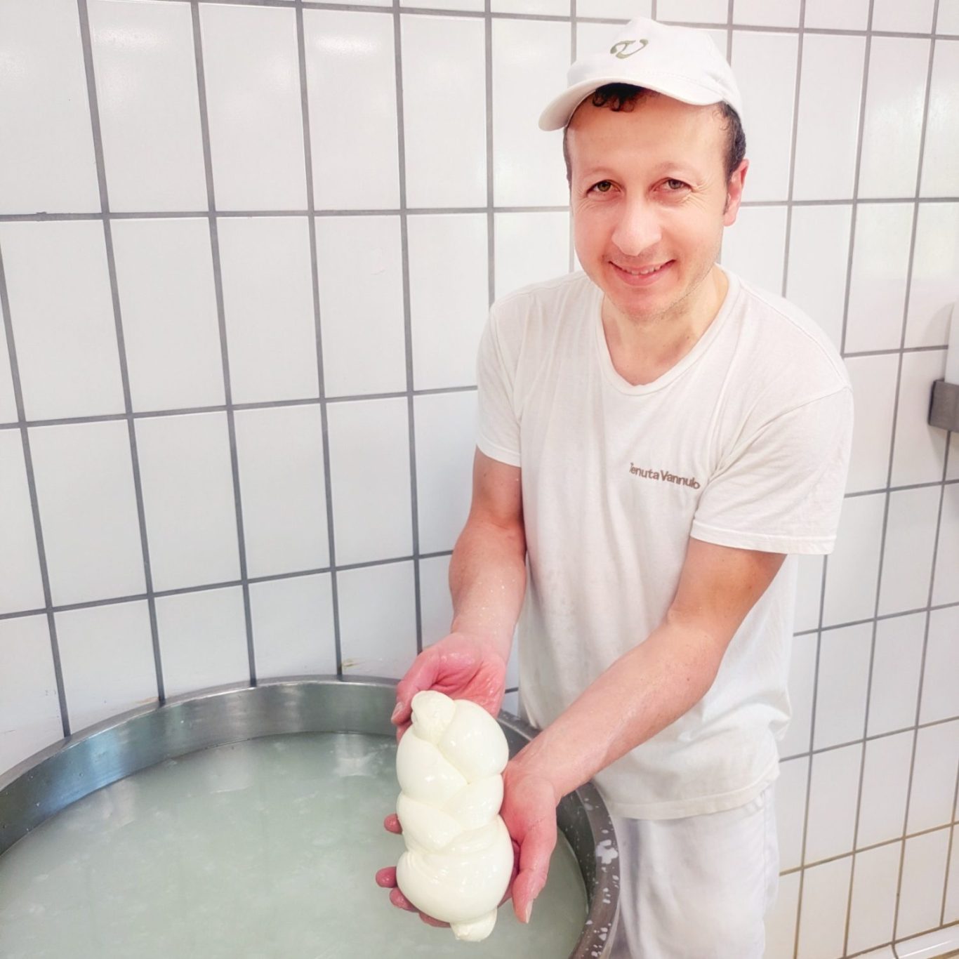 Käser der Tenuta Vannulo hält strahlend einen frisch geflochtenen Mozzarella-Zopf in der Käserei. Mit sichtbarem Stolz präsentiert Michele den noch warmen Mozzarella-Zopf – Sinnbild für das handwerkliche Herz der Tenuta Vannulo.